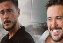 Two men posing together outdoors: one with a beard and serious look, the other smiling broadly with white teeth in front of a glass railing and skyline background.