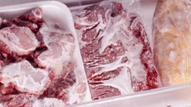 Frozen raw beef cuts in white Styrofoam trays, heavily frosted and stored in a freezer.