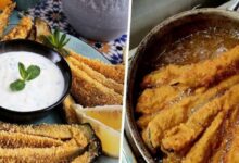 Crispy breaded zucchini sticks with a creamy herb dip in a black bowl and lemon wedges on a decorative plate.
