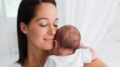 Mother cradling a newborn baby close to her shoulder, both eyes closed in a tender, peaceful moment.