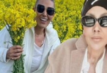 Two women wearing sunglasses pose in a bright yellow canola field; one holds a bouquet of yellow blooms.