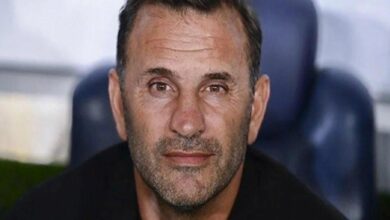 Close-up portrait of a middle-aged man with short dark hair and stubble, looking at the camera with a neutral expression.