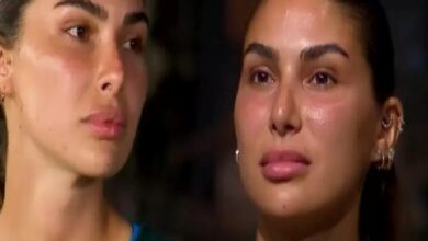 Two women with dark hair and glowing skin sit side by side, looking off to the left with serious expressions in a dim setting.