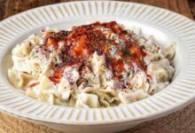 Creamy white pasta on a decorative plate, sprinkled with herbs and red chili flakes on top.