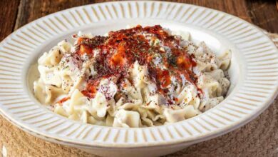 Creamy white pasta on a decorative plate, sprinkled with herbs and red chili flakes on top.